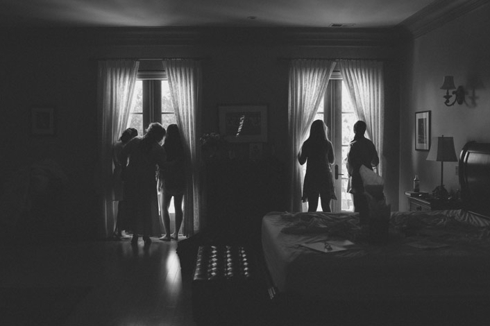 black and white of bridal party sneaking a peak of the guest arriving to the wedidng
