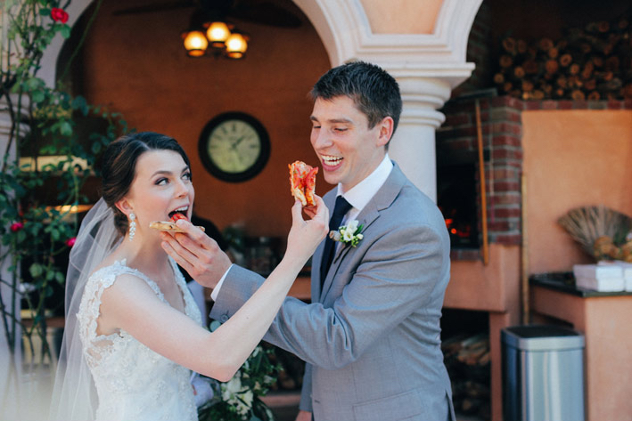 bride and groom feeding each other pizza and smiling 